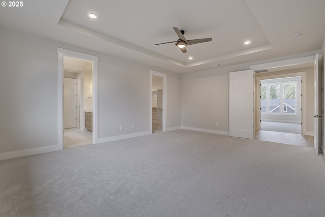 unfurnished bedroom with light carpet, a tray ceiling, and baseboards
