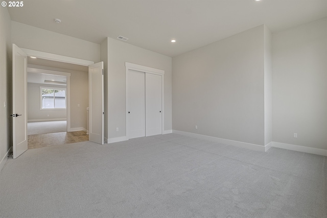 unfurnished bedroom with a closet, light carpet, baseboards, and visible vents