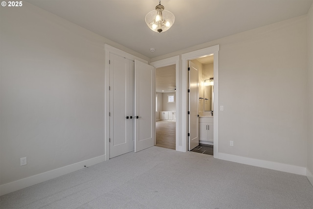 unfurnished bedroom with baseboards, ensuite bath, and carpet