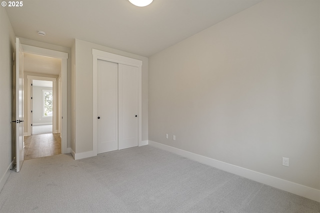 unfurnished bedroom featuring baseboards, a closet, and light carpet