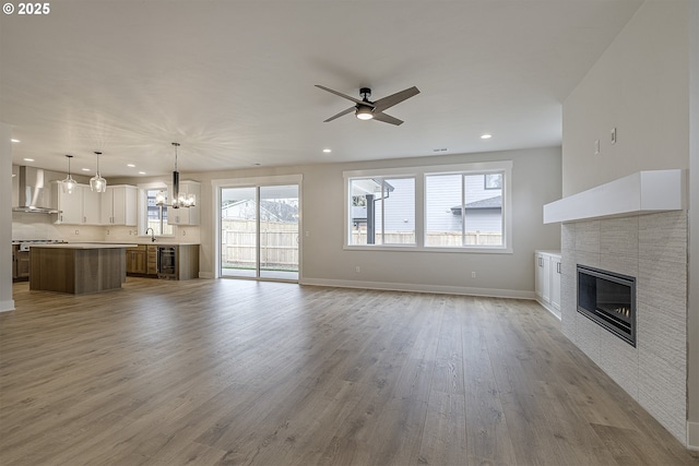 unfurnished living room with recessed lighting, ceiling fan with notable chandelier, baseboards, a tiled fireplace, and wood finished floors