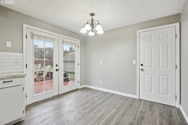 unfurnished dining area with a textured ceiling, french doors, wood finished floors, and baseboards