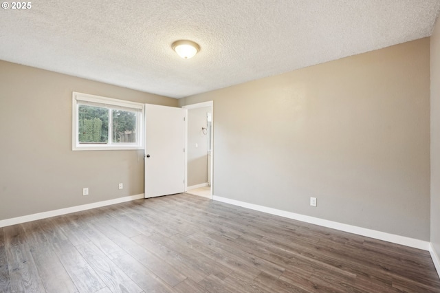 spare room with a textured ceiling, baseboards, and wood finished floors