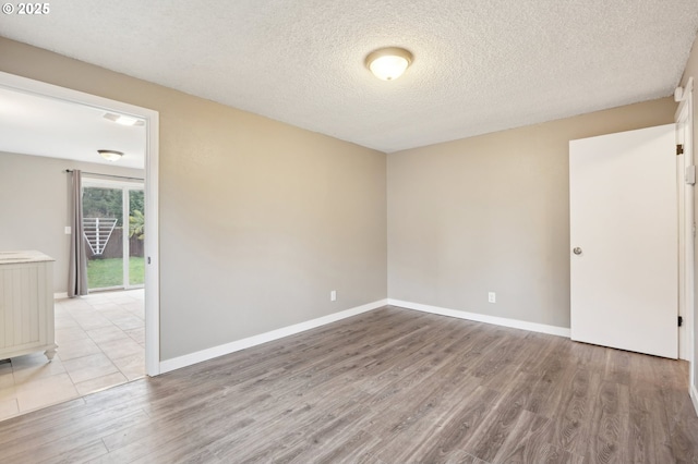 spare room featuring a textured ceiling, light wood-type flooring, and baseboards