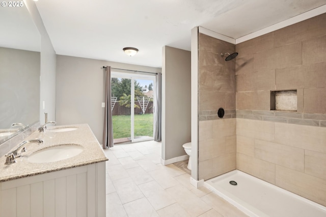 bathroom featuring baseboards, tiled shower, a sink, and toilet