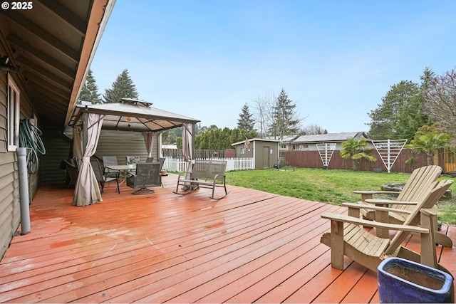 wooden terrace featuring a fenced backyard, an outdoor structure, a gazebo, a storage unit, and outdoor dining space