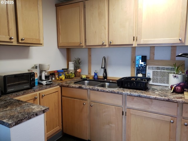 kitchen with backsplash, light brown cabinetry, dark stone counters, and a sink