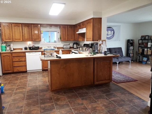 kitchen featuring a peninsula, open floor plan, white appliances, brown cabinetry, and under cabinet range hood