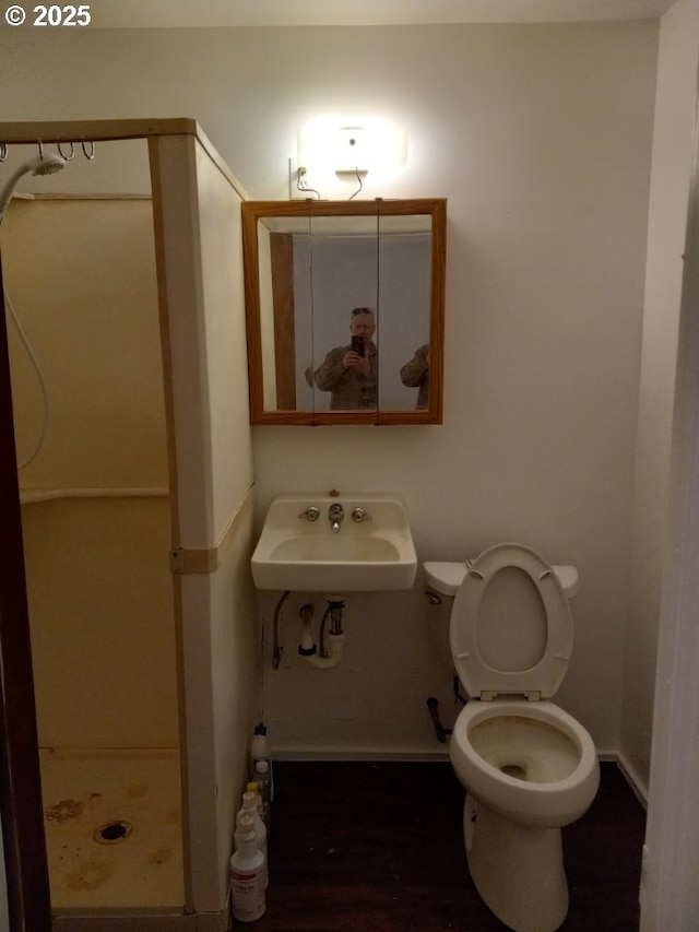 bathroom featuring wood finished floors, toilet, a sink, baseboards, and a stall shower