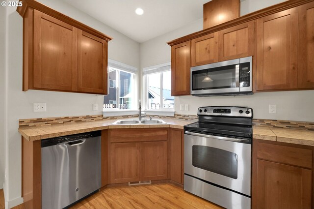kitchen with a sink, light wood-style flooring, brown cabinets, and appliances with stainless steel finishes