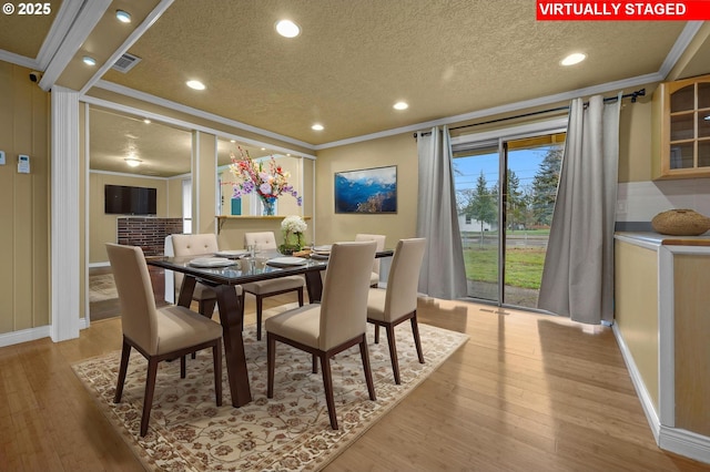 dining area featuring light wood-type flooring, a textured ceiling, visible vents, and ornamental molding