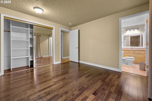 unfurnished bedroom featuring dark wood-type flooring, baseboards, ensuite bathroom, a closet, and a textured ceiling