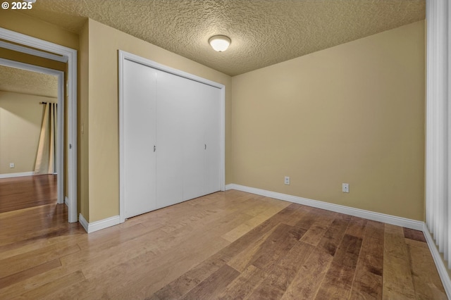 unfurnished bedroom featuring a closet, a textured ceiling, baseboards, and wood finished floors