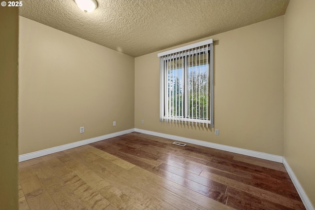 empty room with hardwood / wood-style floors, baseboards, visible vents, and a textured ceiling