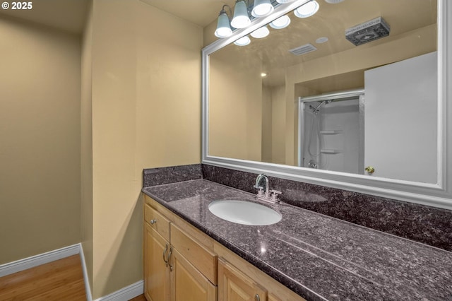 bathroom with vanity, wood finished floors, a shower with shower door, baseboards, and visible vents