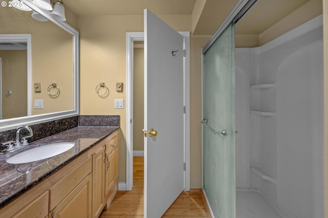 full bath featuring a shower stall, vanity, baseboards, and wood finished floors