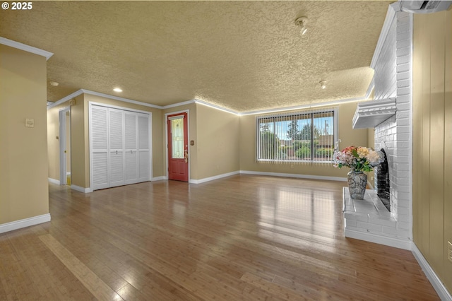 unfurnished living room featuring a brick fireplace, baseboards, ornamental molding, wood finished floors, and a textured ceiling