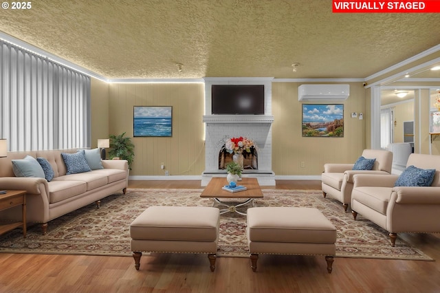 living area featuring wood finished floors, ornamental molding, a wall mounted air conditioner, a textured ceiling, and a brick fireplace