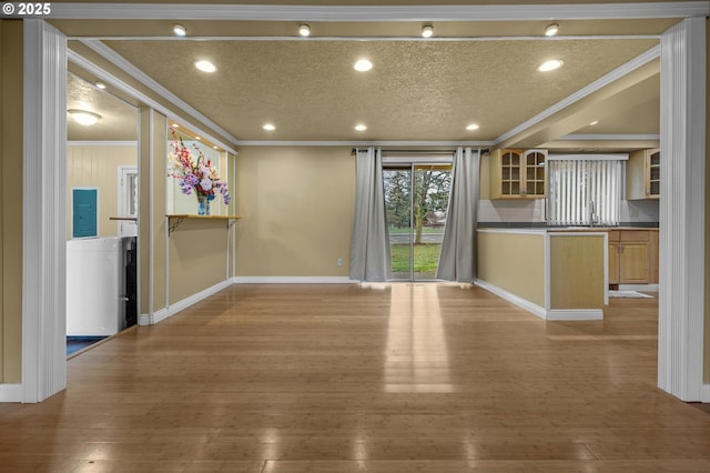 unfurnished living room featuring baseboards, a textured ceiling, light wood-style flooring, and ornamental molding