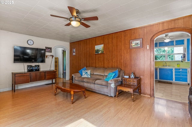 living room with sink, light hardwood / wood-style floors, ceiling fan, and wood walls