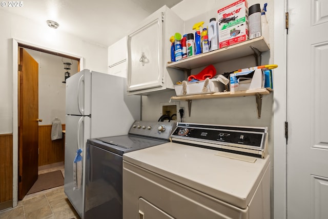 clothes washing area featuring cabinet space, washer and clothes dryer, wooden walls, and wainscoting