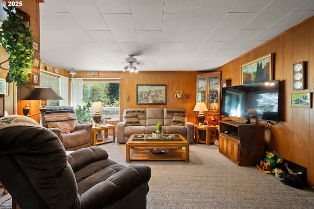 carpeted living area with wood walls and a ceiling fan