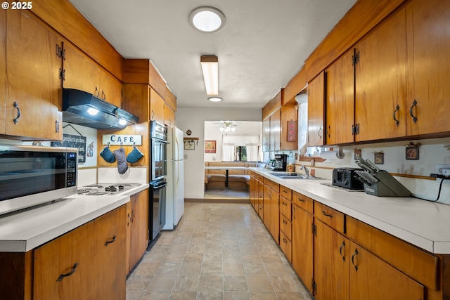 kitchen featuring white appliances, under cabinet range hood, light countertops, a sink, and brown cabinetry
