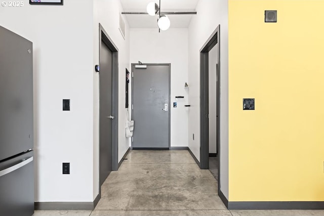 corridor featuring concrete flooring and baseboards