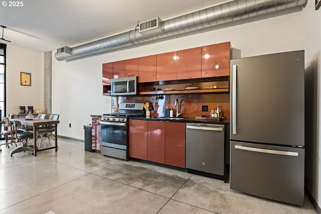 kitchen with stainless steel appliances, dark countertops, visible vents, a sink, and concrete flooring