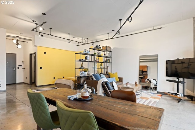 dining space featuring finished concrete floors, rail lighting, a towering ceiling, and baseboards