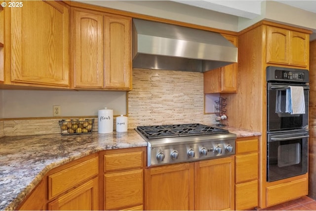 kitchen with dobule oven black, stainless steel gas cooktop, light stone countertops, wall chimney exhaust hood, and backsplash