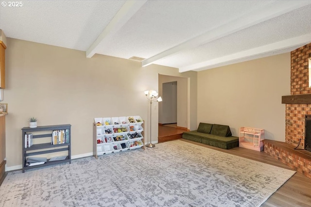 playroom featuring baseboards, a textured ceiling, beam ceiling, visible vents, and a fireplace
