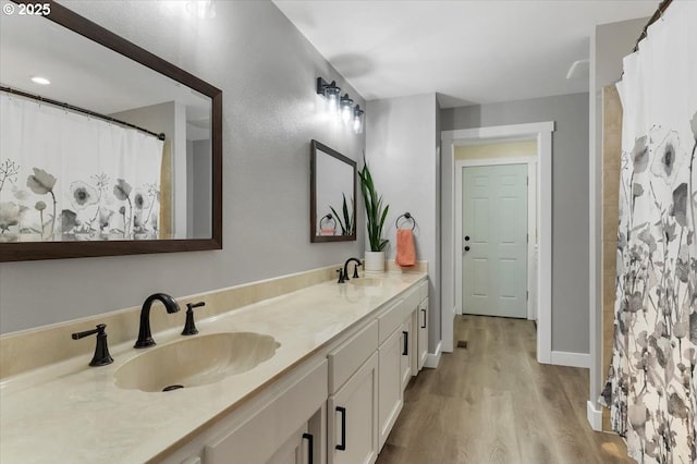 full bathroom with double vanity, wood finished floors, baseboards, and a sink
