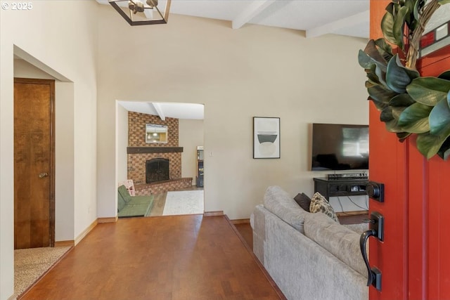 living area featuring a brick fireplace, beam ceiling, baseboards, and wood finished floors