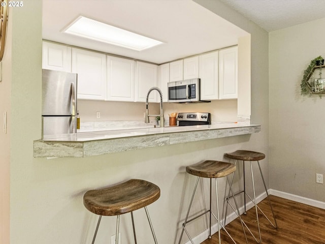 9908 SE Talbert St, Clackamas, OR 97015 - kitchen with appliances with stainless steel finishes, dark wood finished floors, white cabinets, a kitchen bar, and light countertops