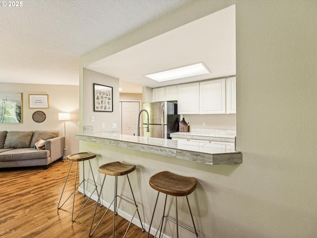 9908 SE Talbert St, Clackamas, OR 97015 - kitchen with freestanding refrigerator, wood finished floors, a kitchen bar, white cabinets, and a textured ceiling