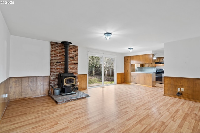 unfurnished living room featuring wooden walls, light hardwood / wood-style flooring, and a wood stove