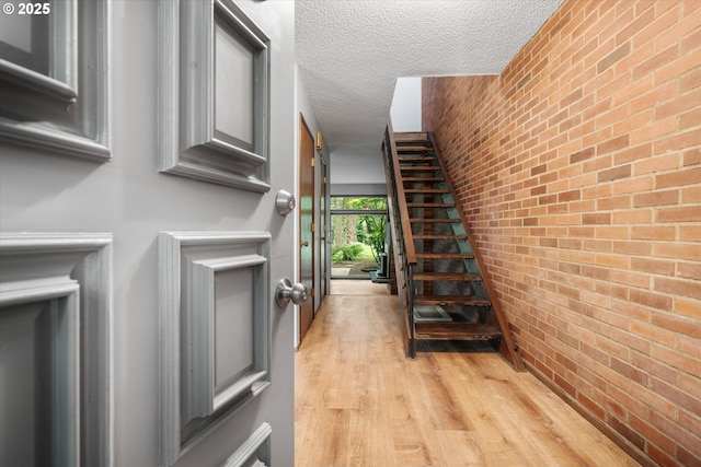 corridor featuring light wood finished floors, a textured ceiling, and brick wall