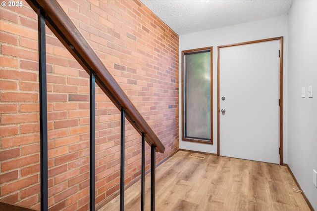 foyer featuring light wood-style flooring, a textured ceiling, baseboards, and brick wall