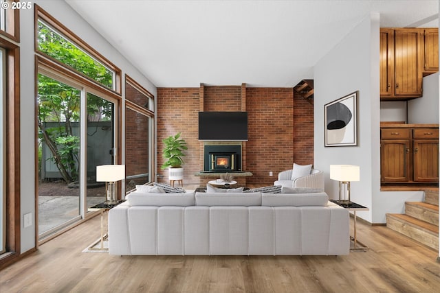 living area with a brick fireplace, light wood-style flooring, baseboards, stairway, and brick wall