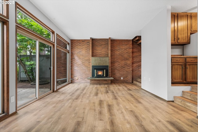 unfurnished living room featuring light wood-type flooring, a large fireplace, brick wall, stairway, and baseboards