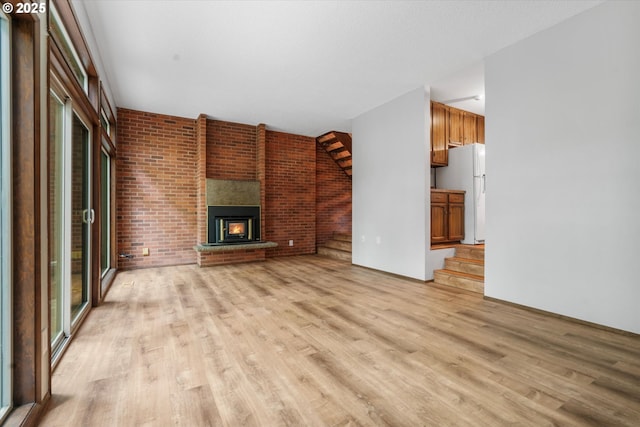 unfurnished living room with light wood-type flooring, a brick fireplace, and brick wall