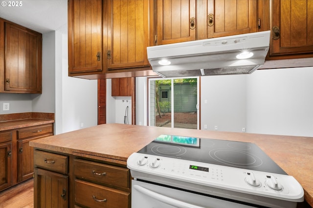 kitchen featuring white range with electric stovetop, under cabinet range hood, and brown cabinets
