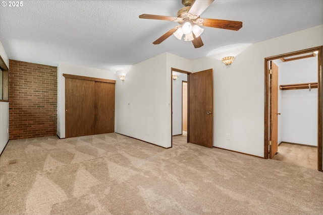 unfurnished bedroom with carpet floors, a textured ceiling, ceiling fan, a closet, and brick wall