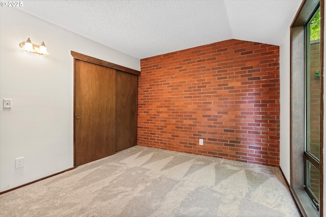 unfurnished bedroom featuring a closet, vaulted ceiling, a textured ceiling, carpet, and brick wall