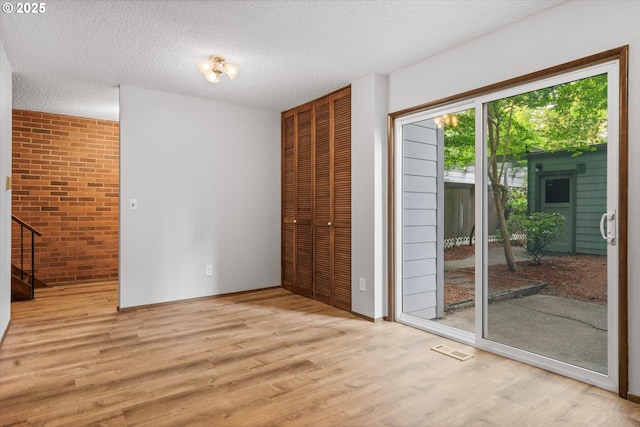 unfurnished bedroom featuring access to exterior, a closet, wood finished floors, a textured ceiling, and brick wall