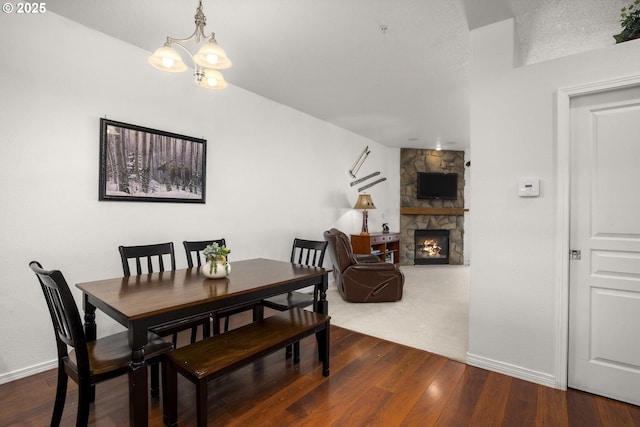 dining area with baseboards, dark wood-style flooring, a stone fireplace, and a notable chandelier