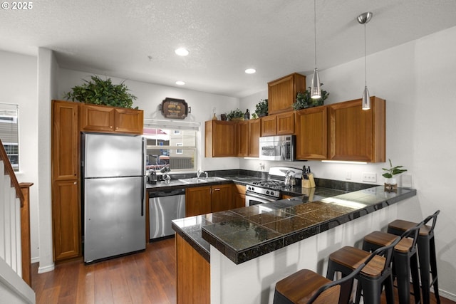 kitchen featuring a peninsula, appliances with stainless steel finishes, tile counters, and brown cabinets