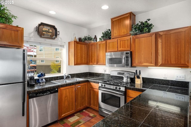 kitchen with brown cabinets, stainless steel appliances, tile countertops, and a sink