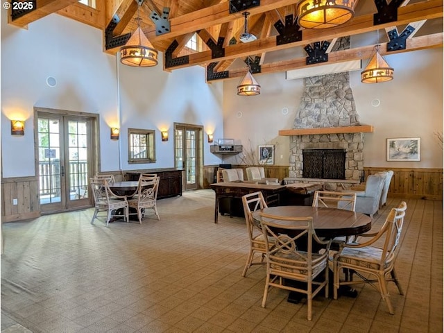 carpeted dining space featuring a fireplace, high vaulted ceiling, beam ceiling, and a wainscoted wall